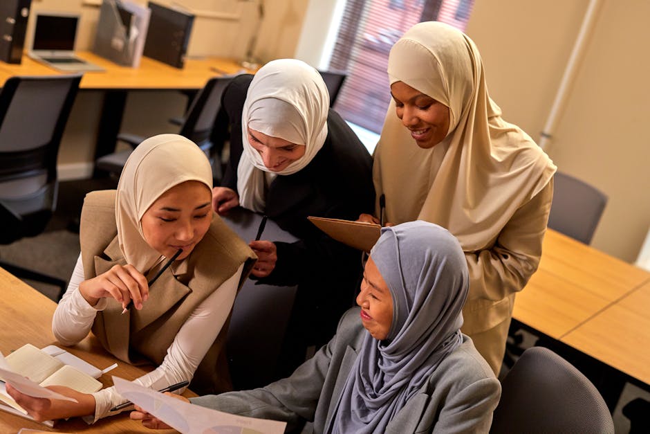 Four diverse women in hijabs engaged in a lively discussion around work documents in a modern office.